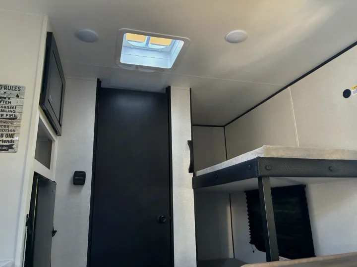 RV rental interior featuring comfortable bunk beds, a TV, a ceiling skylight, and a door. Perfect for a cozy stay.. Jayco 1UJBC0AJ6F7750334 2026