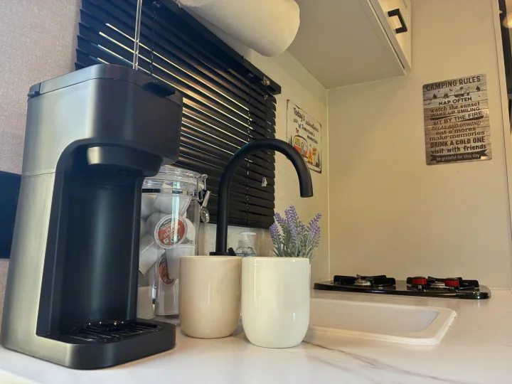An RV rental kitchenette features a coffee maker, K-cups, sink, stove, and charming camping decor.. Jayco 1UJBC0AJ6F7750334 2026