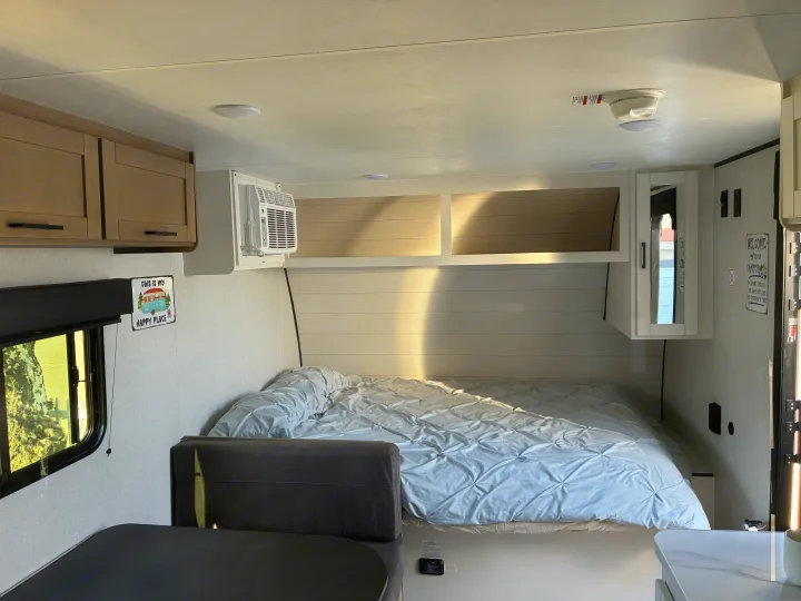 Bright rv rental interior: a cozy bed with blue comforter, small dinette, AC unit, and cheerful wall decor.. Jayco 1UJBC0AJ6F7750334 2026