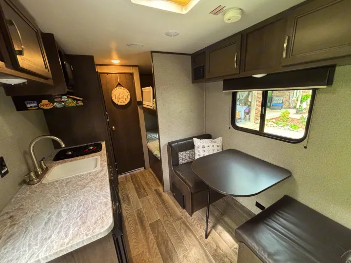 RV rental interior: kitchen with sink & stovetop on left, dinette with window on right, bunk beds in back.. Jayco Jay Flight SLX 2021