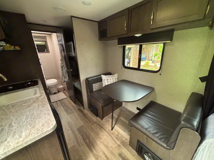 RV rental interior: compact kitchen sink, dinette with table & benches, and a peek into the bathroom with toilet.. Jayco Jay Flight SLX 2021