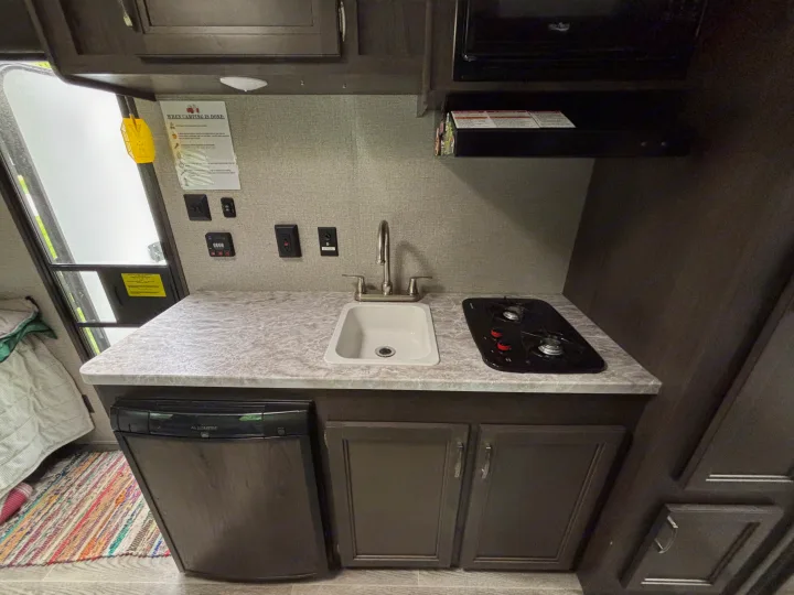 RV rental interior: A compact kitchenette with a sink, two-burner stove, small fridge, and overhead/under-counter storage cabinets.. Jayco Jay Flight SLX 2021