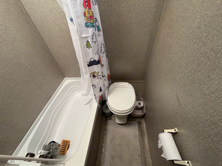 RV rental bathroom featuring a compact tub/shower with a fun camping-themed curtain, toilet, and simple wall decor.. Jayco Jay Flight SLX 2021