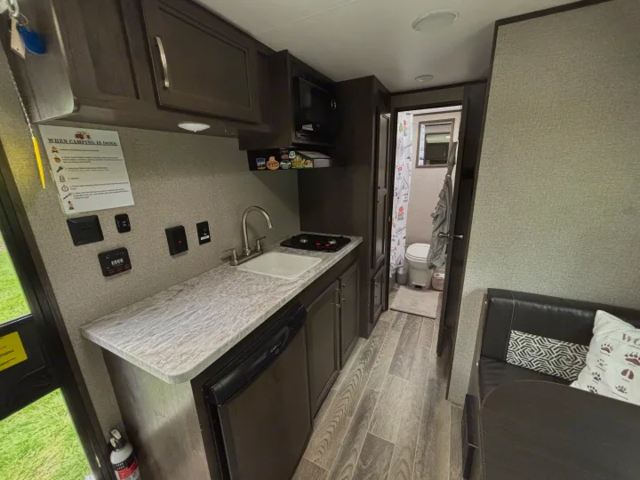 This rv rental's compact interior shows a kitchen with a sink, stove, microwave, a visible bathroom, and dinette seating.. Jayco Jay Flight SLX 2021