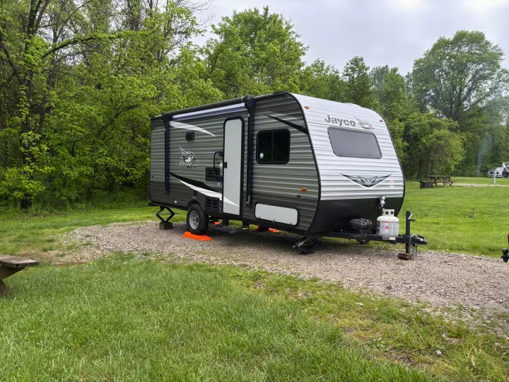 A Jayco travel trailer RV rental, leveled on a gravel pad amidst lush green trees at a serene campground.. Jayco Jay Flight SLX 2021