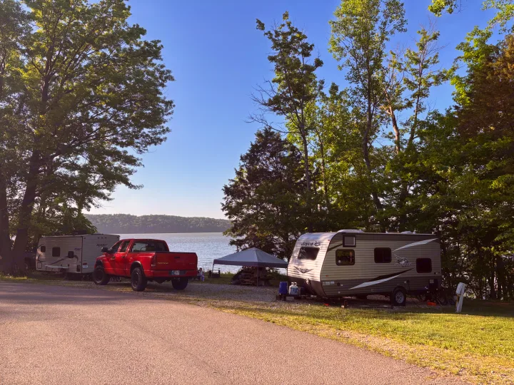 Enjoy your next RV rental by the lake! Two travel trailers and a red pickup truck at a sunny waterside campsite.. Jayco Jay Flight SLX 2021