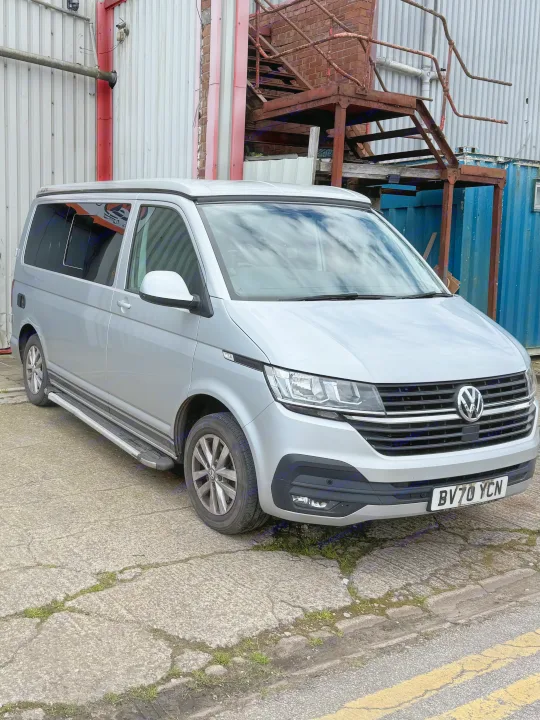 Modern silver VW Transporter camper van with a pop-top, perfect for an RV rental adventure. Parked by an industrial building.. vw Transporter 2020