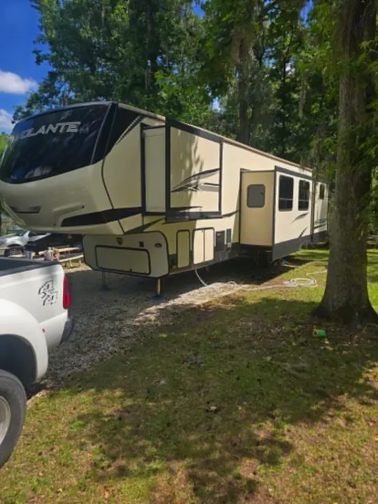 This large cream Volante fifth-wheel RV rental is parked with slide-outs extended in a wooded campground, next to a pickup truck. Perfect for camping.. Crossroads RV Volante 2020