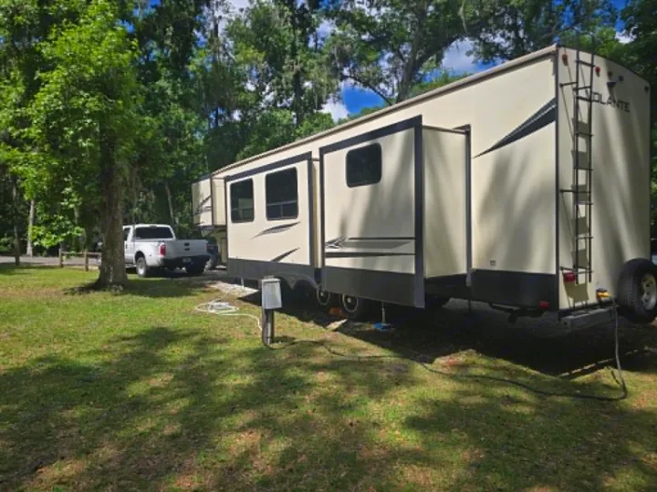 Spacious fifth-wheel **rv rental** parked in a shady, treed campsite with a pickup truck nearby. Perfect for **camping**.. Crossroads RV Volante 2020