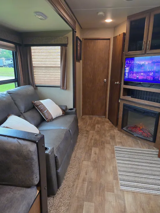 Cozy RV rental living area with a gray sofa, TV, and electric fireplace, offering home-like comfort for your journey.. Grand Design Reflection 2017