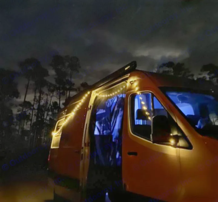 Experience cozy nights with our rv rental! A campervan adorned with warm string lights, blue interior, parked under a dark sky.. Mercedes-Benz Sprinter 2023