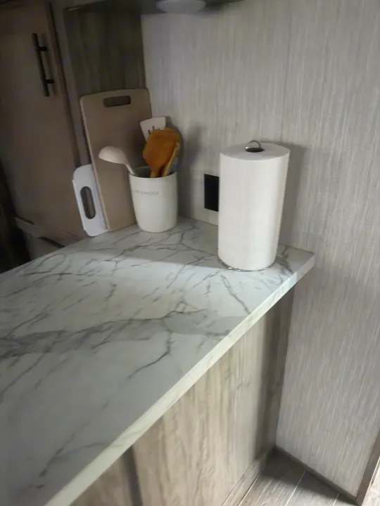 RV rental kitchen featuring a compact counter with marble-look top, paper towels, and a utensil holder.. Forest River Cherokee Arctic Wolf 2020