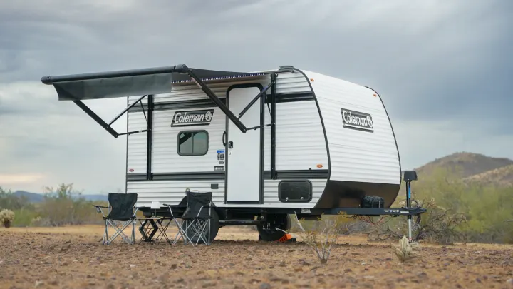 Coleman travel trailer rv rental with an extended awning and chairs set up in a sparse desert landscape under a cloudy sky.. Coleman 13B 2026