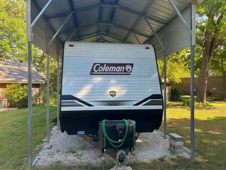 This white & black Coleman travel trailer (RV) is parked under a metal carport, perfect for your next rv rental adventure.. Coleman 270TQ 2022