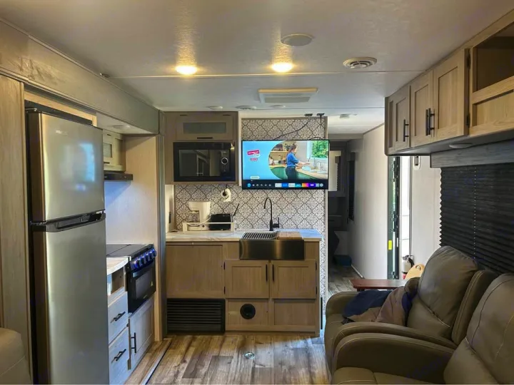 Modern RV rental interior: well-equipped kitchen (fridge, microwave, sink, stove) and cozy living area with recliners.. Coleman 270TQ 2022
