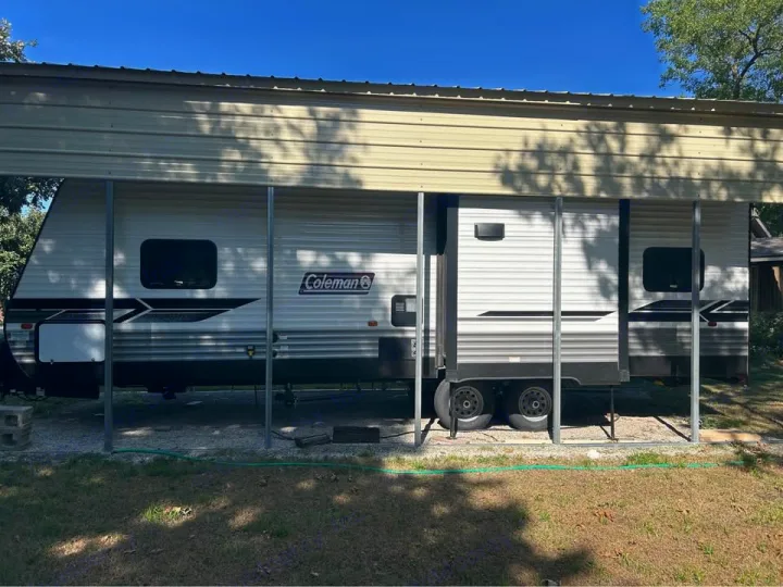 This Coleman travel trailer, ideal for an RV rental, is parked under a carport with its slide-out extended.. Coleman 270TQ 2022