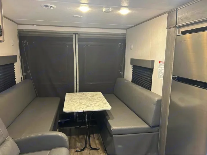 Step inside this RV rental's dining area, featuring comfy gray benches, a marble-top table, and a refrigerator.. Coleman 270TQ 2022