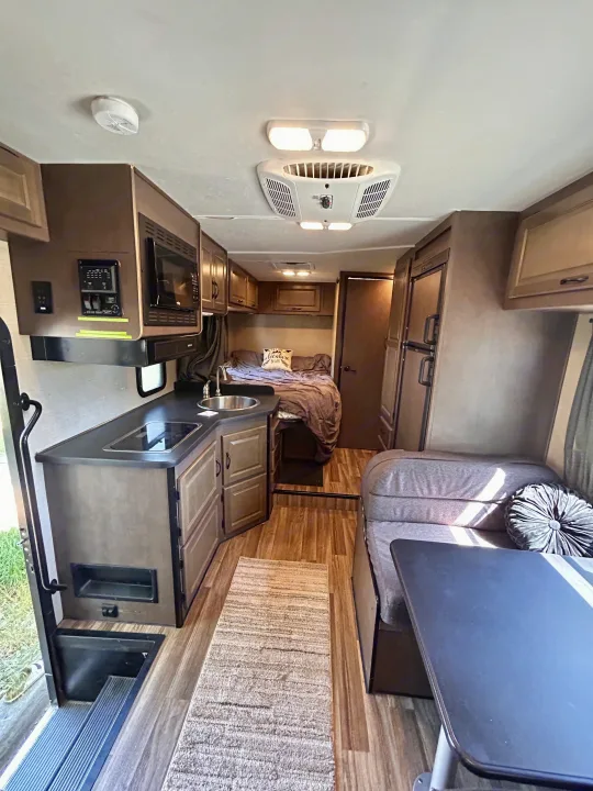 This cozy rv rental interior features a full kitchen with microwave, a rear bed, and a comfortable dinette with table. Fridge & AC also visible.. Thor Majestic 2018