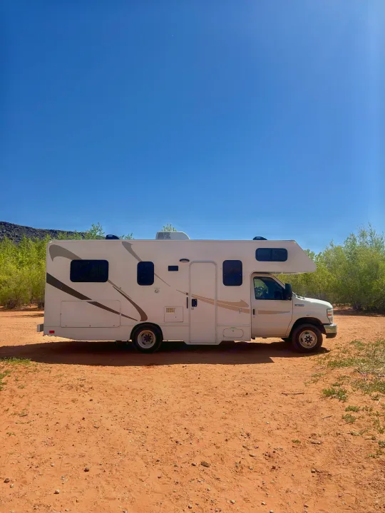 This white RV rental is parked on red desert dirt under a clear blue sky, ready for an outdoor adventure or road trip.. Thor Majestic 2018