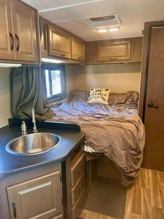 RV rental interior features a snug bedroom with a comfy bed, overhead cabinets, and a compact sink area for easy travel.. Thor Majestic 2018