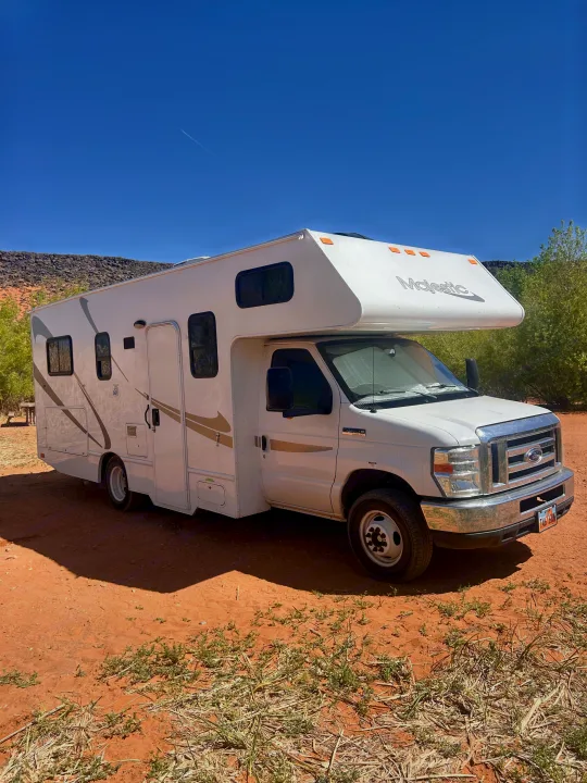 White Majestic RV rental parked on red desert ground under a blue sky, ideal for outdoor travel and camping adventures.. Thor Majestic 2018