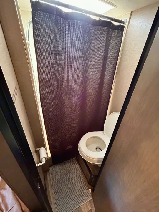 Inside a compact **rv rental** bathroom: a white toilet, dark mesh shower curtain, and small shower area with a mat.. Thor Majestic 2018