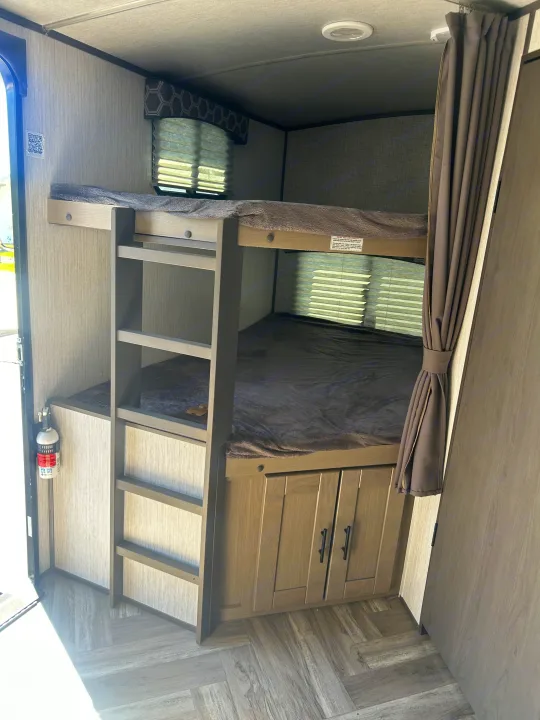 Cozy RV rental interior featuring comfortable bunk beds with a ladder, storage cabinets, and a fire extinguisher.. Cruiser RV Shadow Cruiser 2022