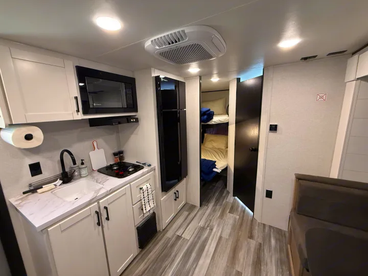 Inside this cozy rv rental, a modern kitchenette with microwave, sink, and fridge sits across from bunk beds, perfect for family trips.. Jayco Jay Flight SLX Baja Edition 2025