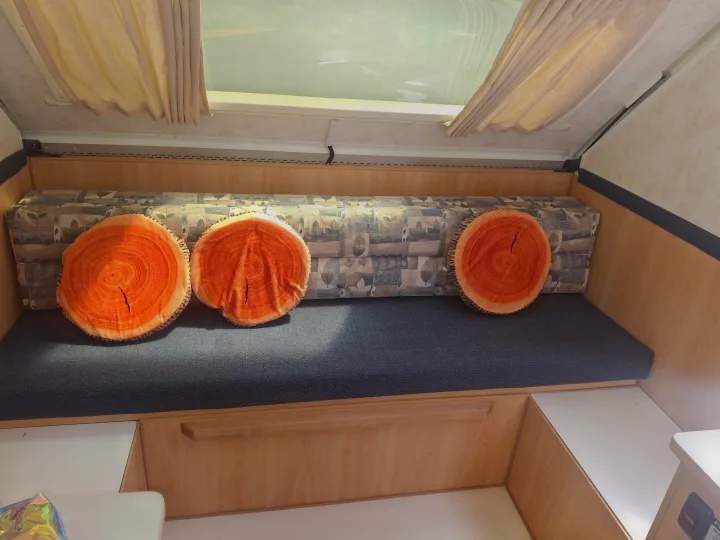 Cozy RV rental interior with bench seating, unique wood-slice pillows, light wood paneling, and a large skylight.. Chalet Chalet Popup Trailer 2006