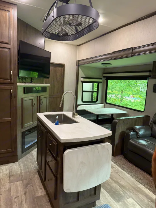 Stylish RV rental interior: kitchen island, cozy dinette, and living area with fireplace & TV. Enjoy green views!. Forest River Sandpiper 2021