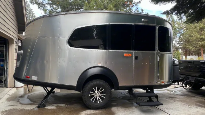 Silver teardrop travel trailer for an rv rental adventure. Off-road tires, sleek design, parked in a driveway next to a home.. Airstream Basecamp 2022