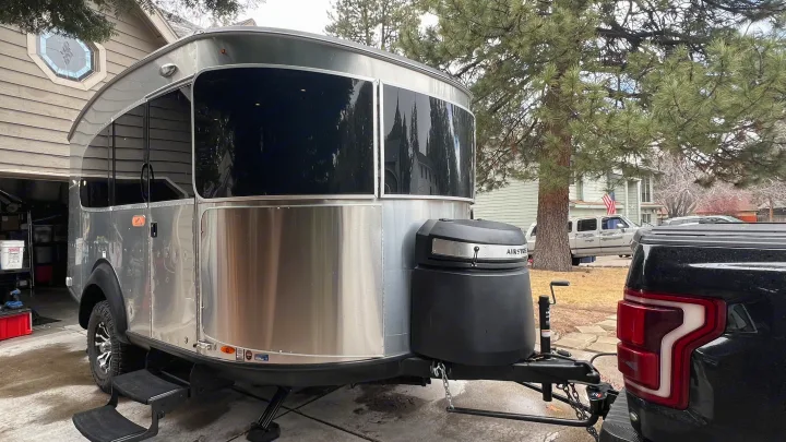 A polished silver Airstream Basecamp travel trailer, ideal for an RV rental, is hitched to a black pickup truck by a home.. Airstream Basecamp 2022