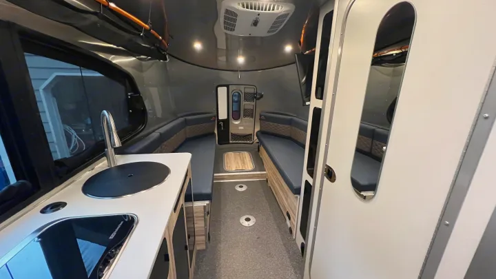 Modern rv rental interior: kitchen, U-shaped seating, TV, & AC. Ideal for road trips, this camper offers compact comfort.. Airstream Basecamp 2022