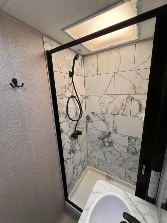 RV rental bathroom features a modern marble-look shower with black fixtures and a sink.. Coachmen Cross Trail 2023