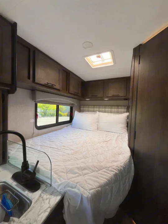 RV rental bedroom: cozy space with bed, sink, overhead cabinets, a window, and a skylight.. Coachmen Cross Trail 2023