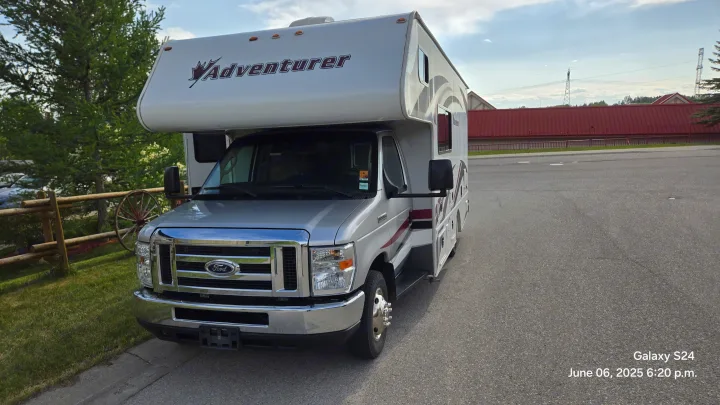 Silver Adventurer Class C RV rental parked on asphalt, featuring a Ford front, grass, wooden fence, and a wagon wheel.. Adventurer Adventurer Motorhome 2017