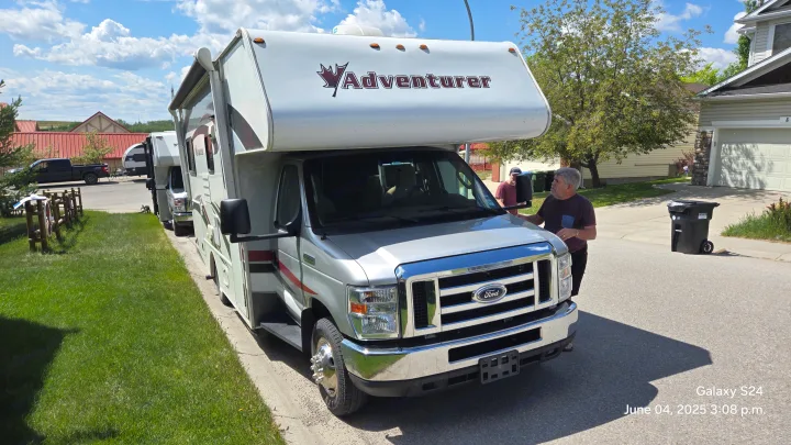 Man inspects a parked Adventurer RV rental on a sunny residential street, with another RV and truck in the background.. Adventurer Adventurer Motorhome 2017