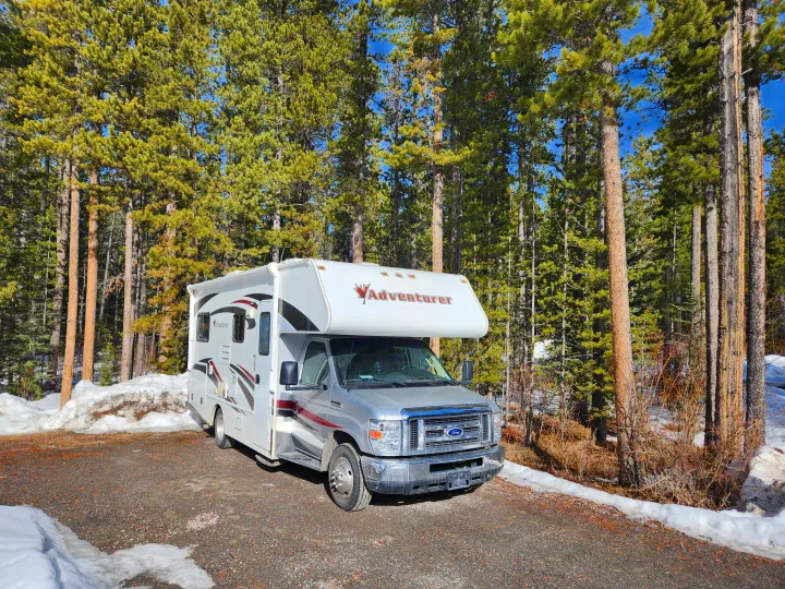 An Adventurer RV rental parked in a snowy forest, surrounded by tall pine trees under a clear blue sky.. Adventurer Adventurer Motorhome 2017