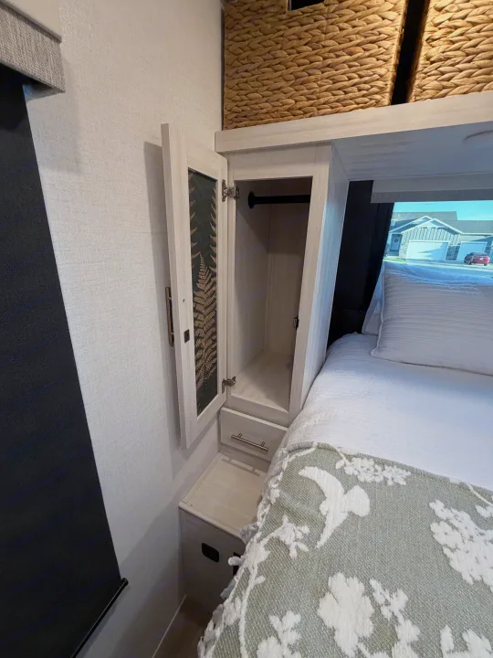 This RV rental bedroom features an open wardrobe, storage baskets, a bed, and a window view, maximizing compact living.. Forest River Unmapped 2026