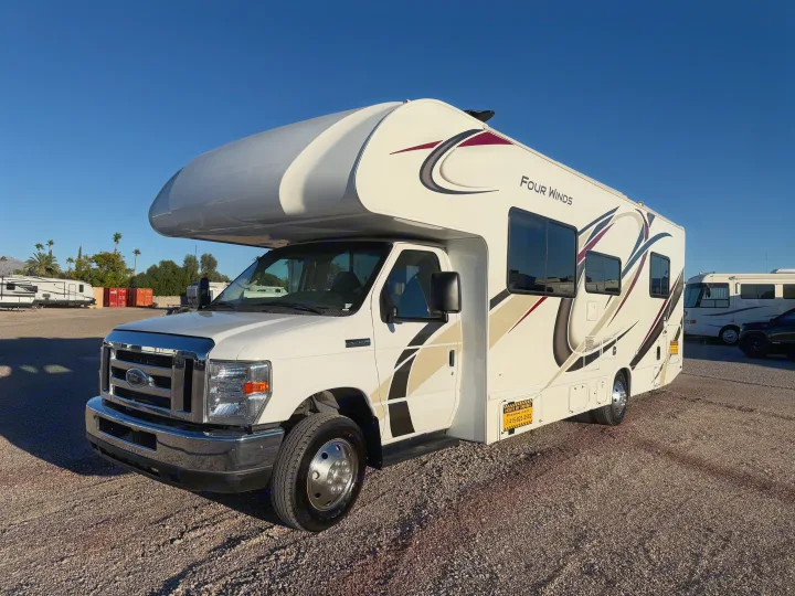 White Four Winds Class C RV rental on a Ford chassis, parked on gravel under a clear blue sky. Ideal recreational vehicle.. Thor Four Winds 2019