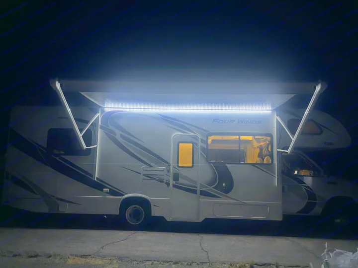 An RV rental shines bright at night with its extended awning and LED strip lights illuminating the side.. Thor Four Winds 2019