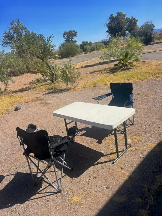 This RV rental campsite features a portable table & two camping chairs on gravel, under a bright blue sky, ready for relaxation.. Thor Four Winds 2019