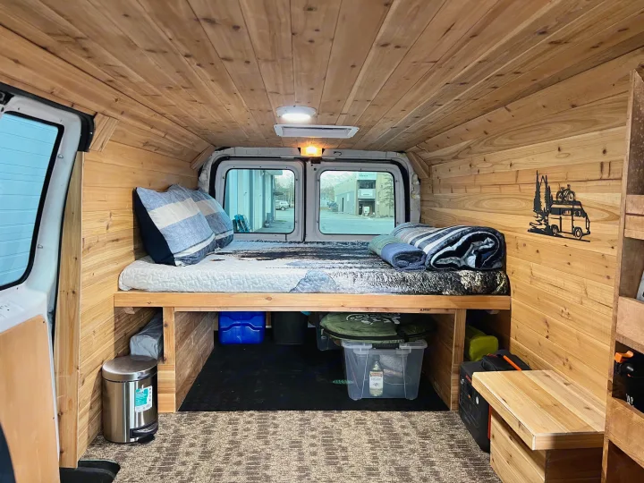 An inviting RV rental van interior with cedar wood paneling, a raised bed, and accessible under-bed storage.. Ford Econolline 250s 2013