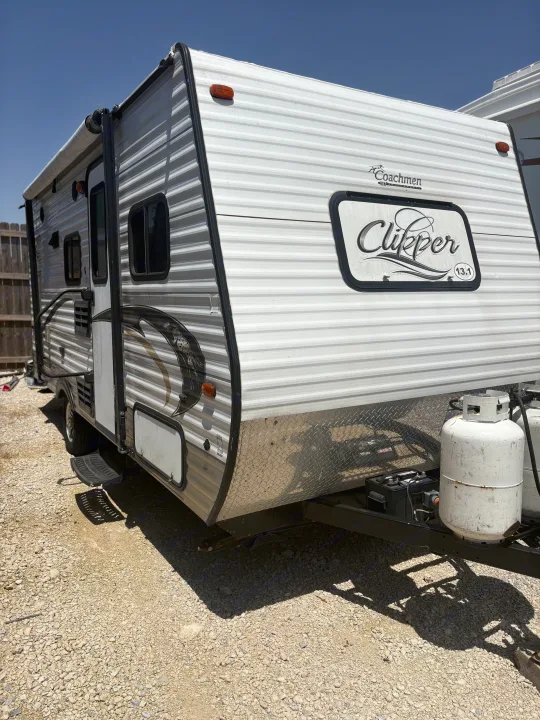 Coachmen Clipper 13.1 travel trailer with white and gray striped siding, awning, and propane tanks. Ideal RV rental.. Coachmen Clipper 17BH 2015