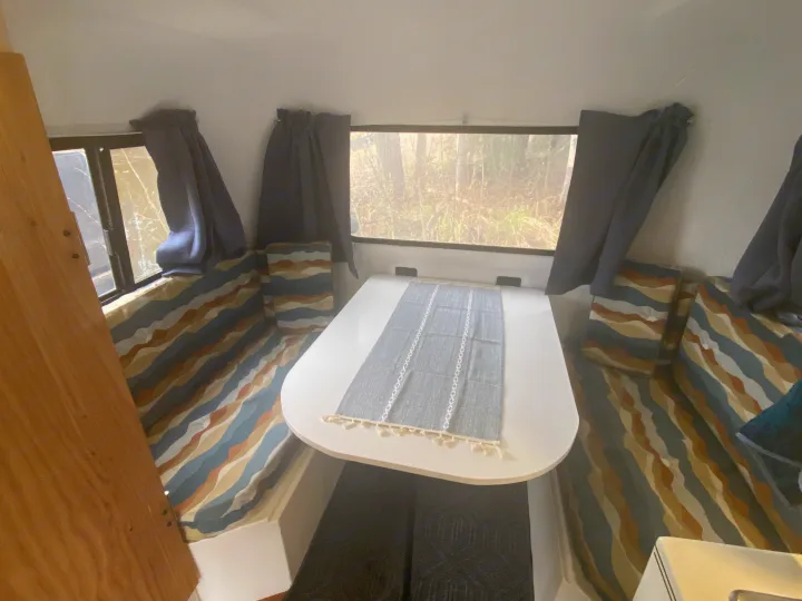 Cozy rv rental interior with a dining table, patterned cushions, and nature views from the windows.. Scamp 13' 1987