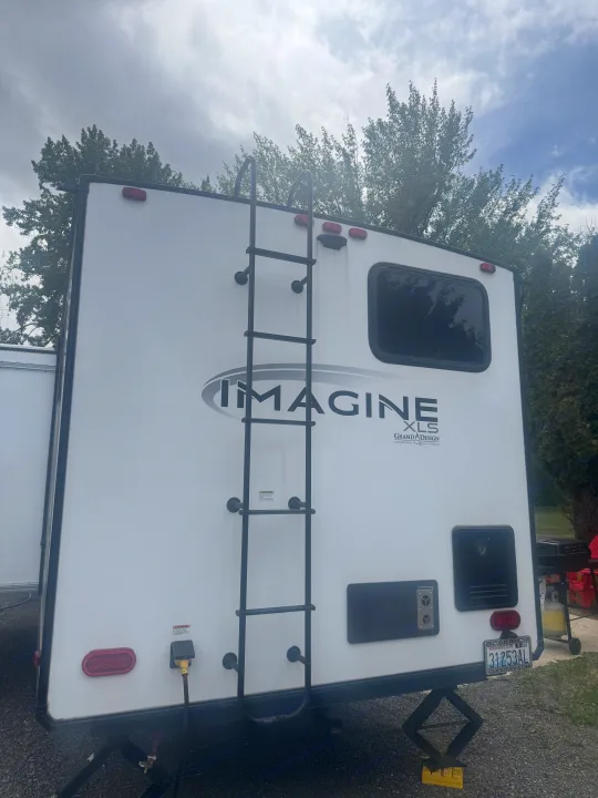 Rear view of a white Imagine XLS Grand Design RV, featuring a ladder, power inlet, and Washington license plate for your next rv rental.. Grand Design Imagine 2024