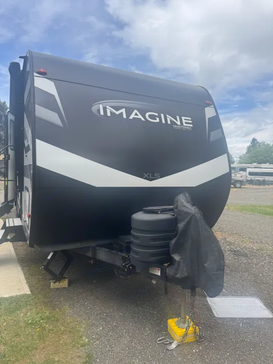This Grand Design Imagine travel trailer, possibly an RV rental, parked on gravel with leveling blocks at a campsite.. Grand Design Imagine 2024