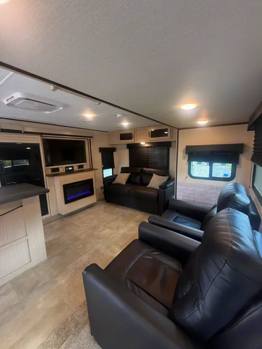 Modern RV rental interior featuring black leather recliners, sofa, electric fireplace, and TV in a cozy living space.. Coachmen Apex 2021