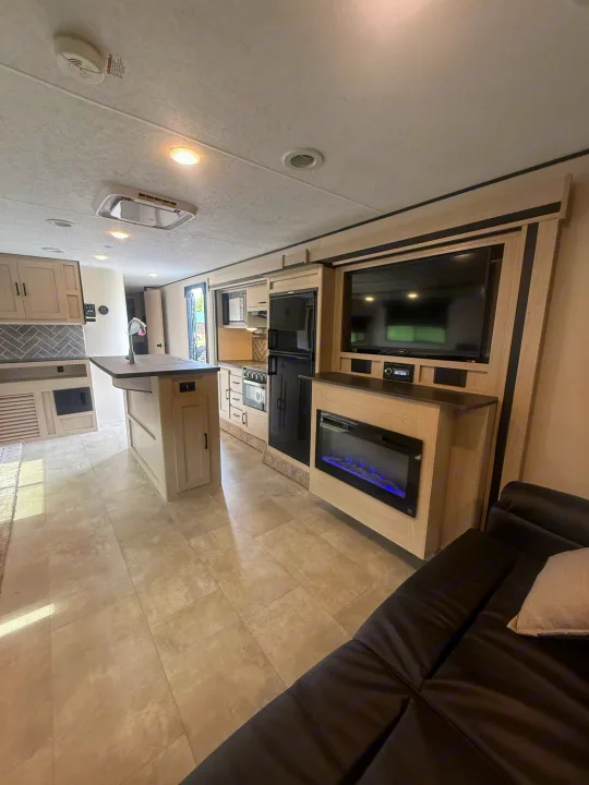 This modern RV rental features a full kitchen with an island, living area with a TV and fireplace, and a comfy dark couch.. Coachmen Apex 2021