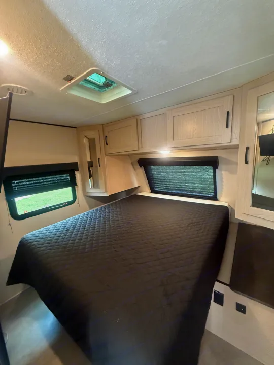 Comfortable RV rental bedroom featuring a large bed, overhead cabinets, windows with blinds, and a ceiling vent.. Coachmen Apex 2021